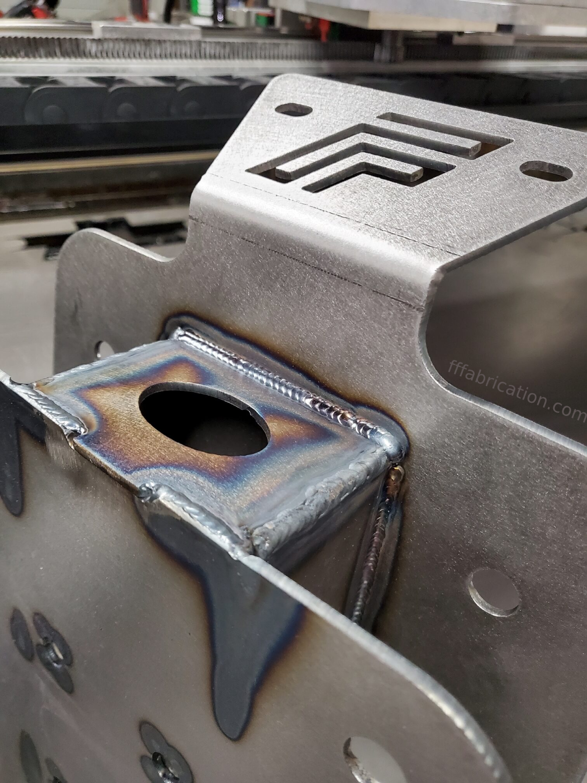 Metal component with text 'fabrication.com' on a workshop background