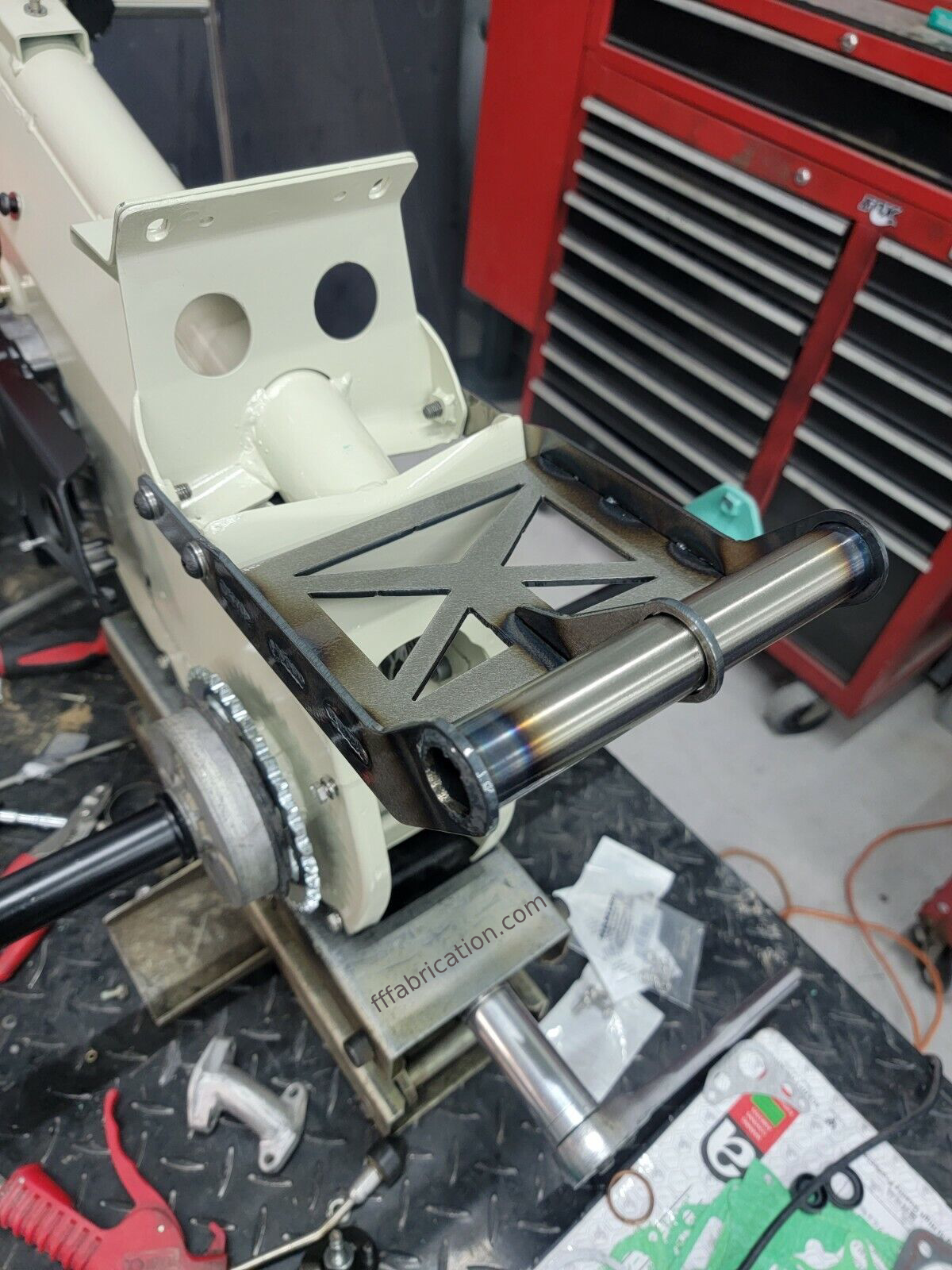 Metal bracket or component on a workbench with tools and equipment in the background