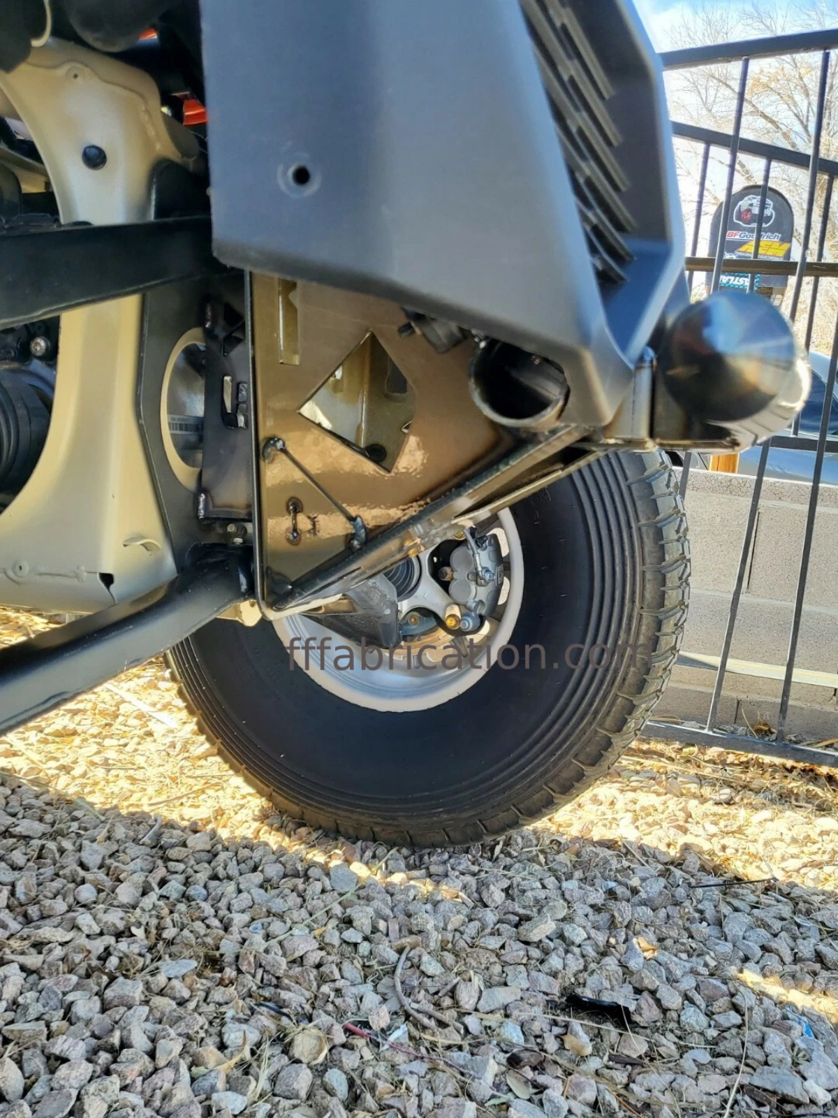 Close-up of a can-am wheel and suspension system on a gravel surface.
