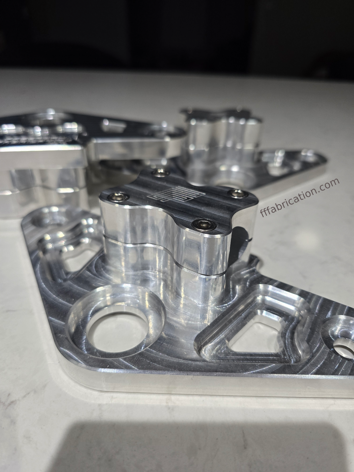 Metal mechanical component on a reflective surface with 'fffabrication.com' branding.