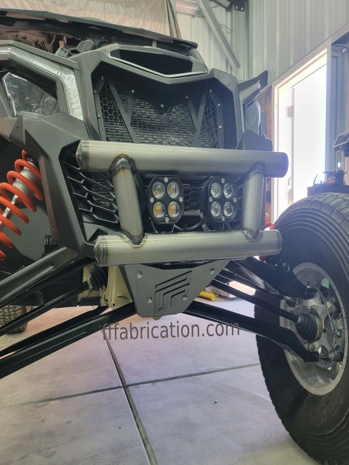 Close-up of a vehicle's front bumper with lights and suspension system in a garage.