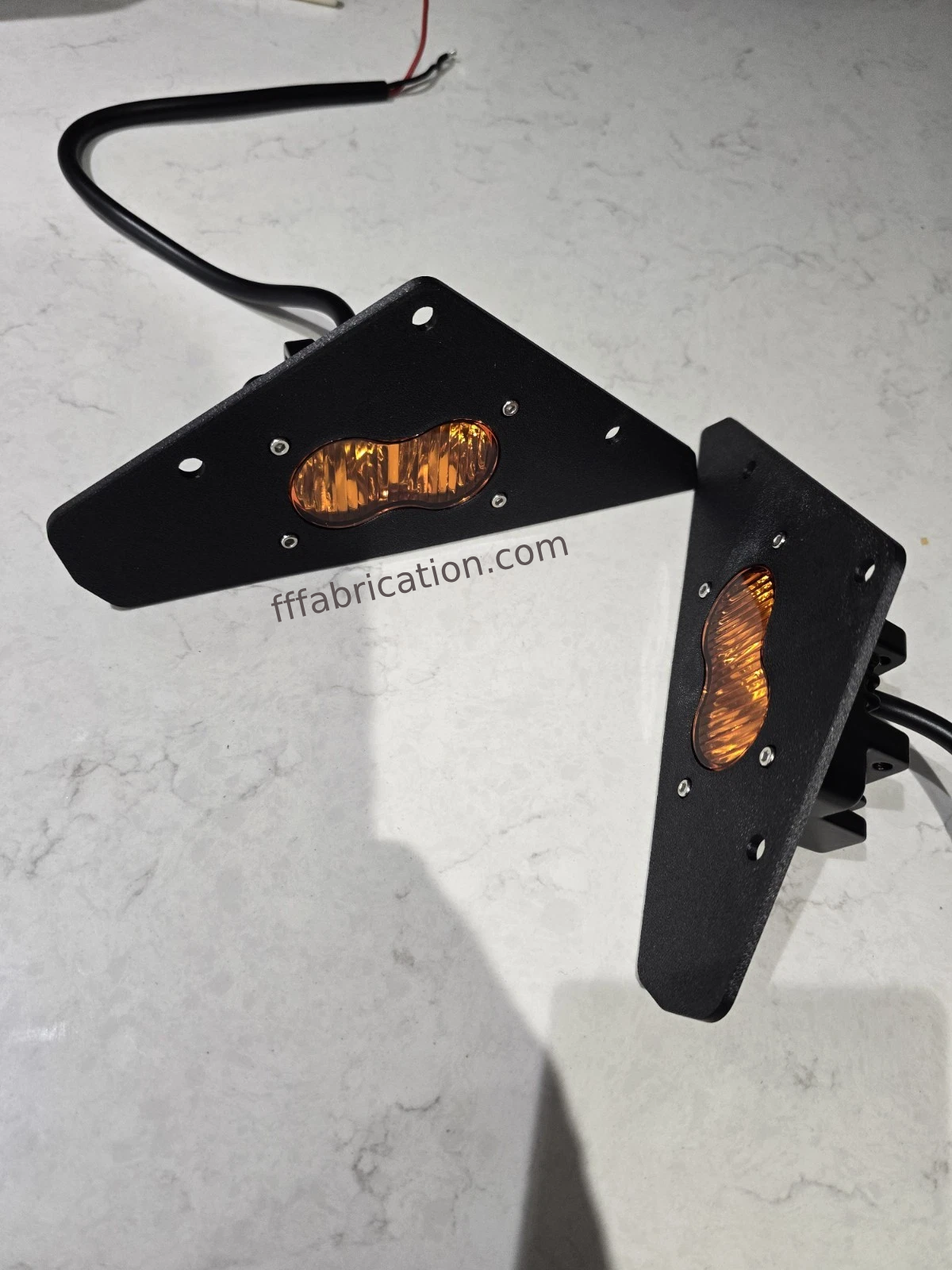 Two amber LED lights with black brackets on a light gray surface, branded 'fffabrication.com'.