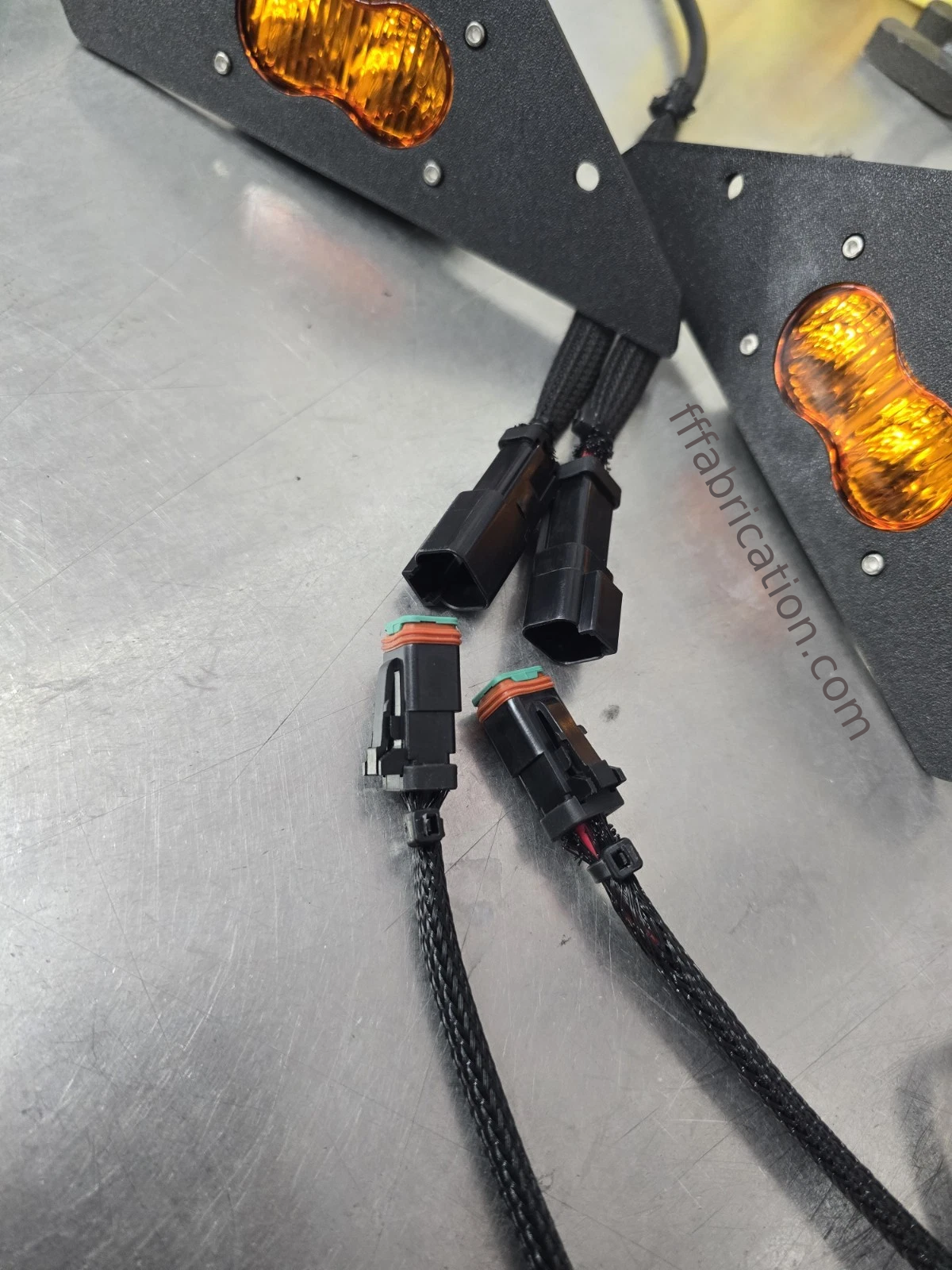 Two turn signals with wiring on a metallic surface, featuring the brand 'tffabrication.com'.