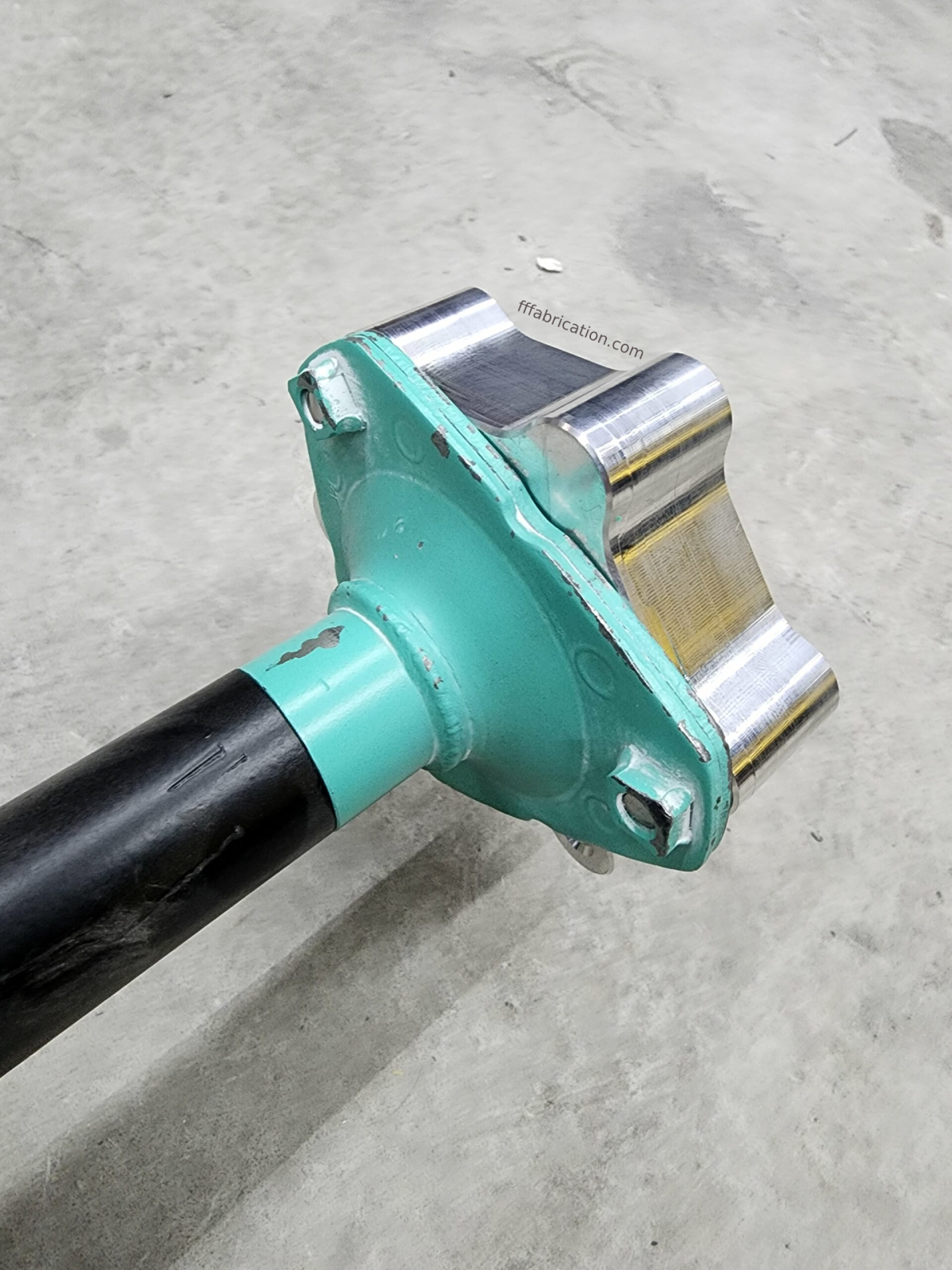 Green and black tool with metal blade on a gray concrete surface