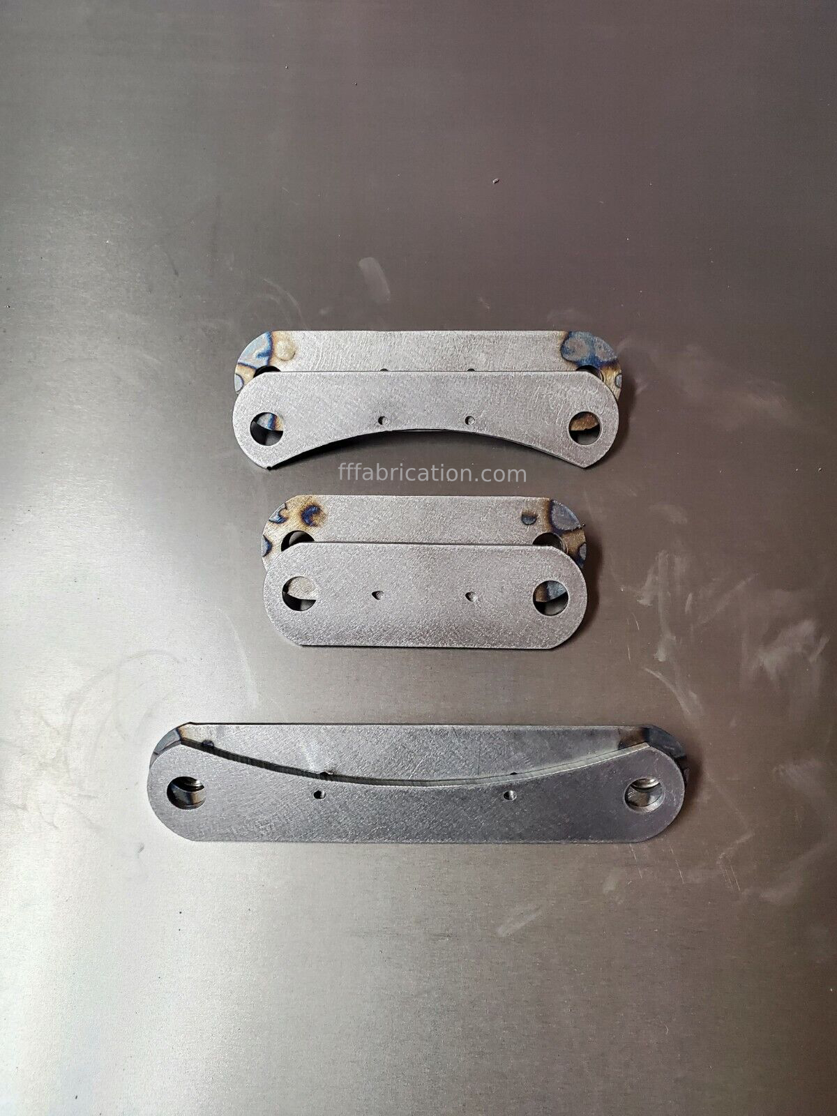 Three metal brackets on a metallic surface with 'tffabrication.com' visible.