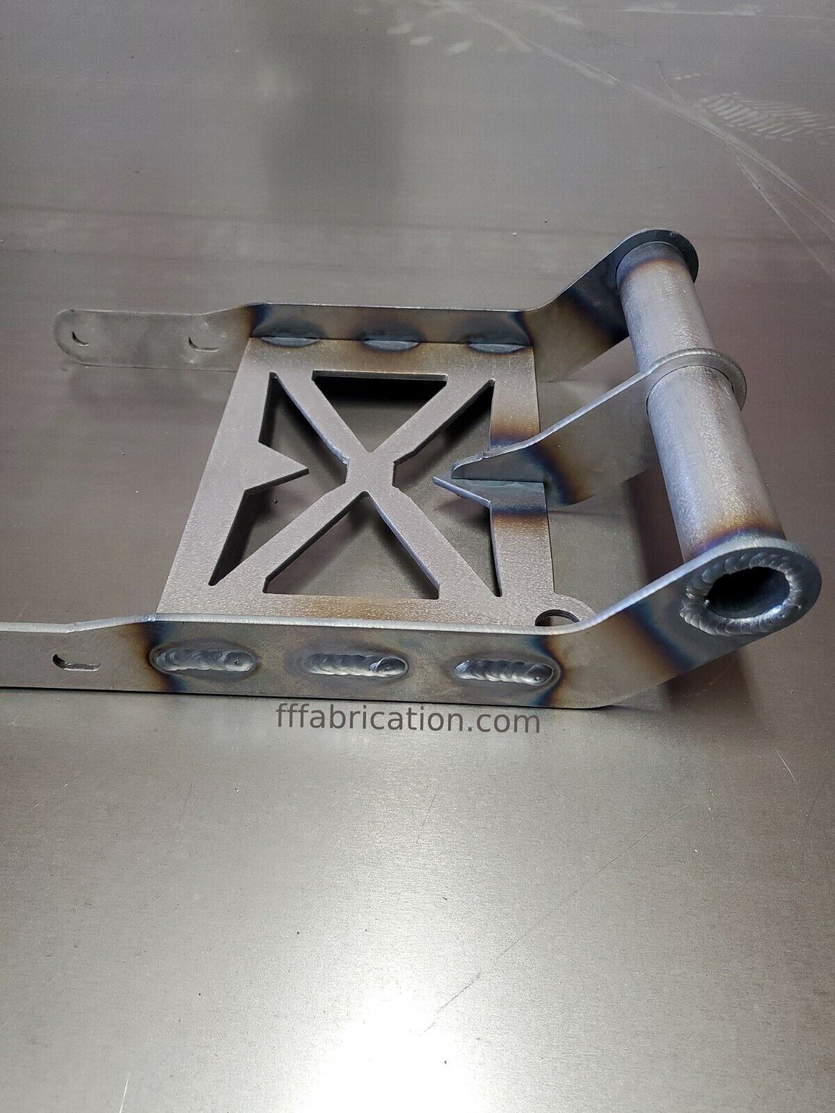 Metal bracket with cut-out design on a metallic surface, featuring 'fffabrication.com' branding.