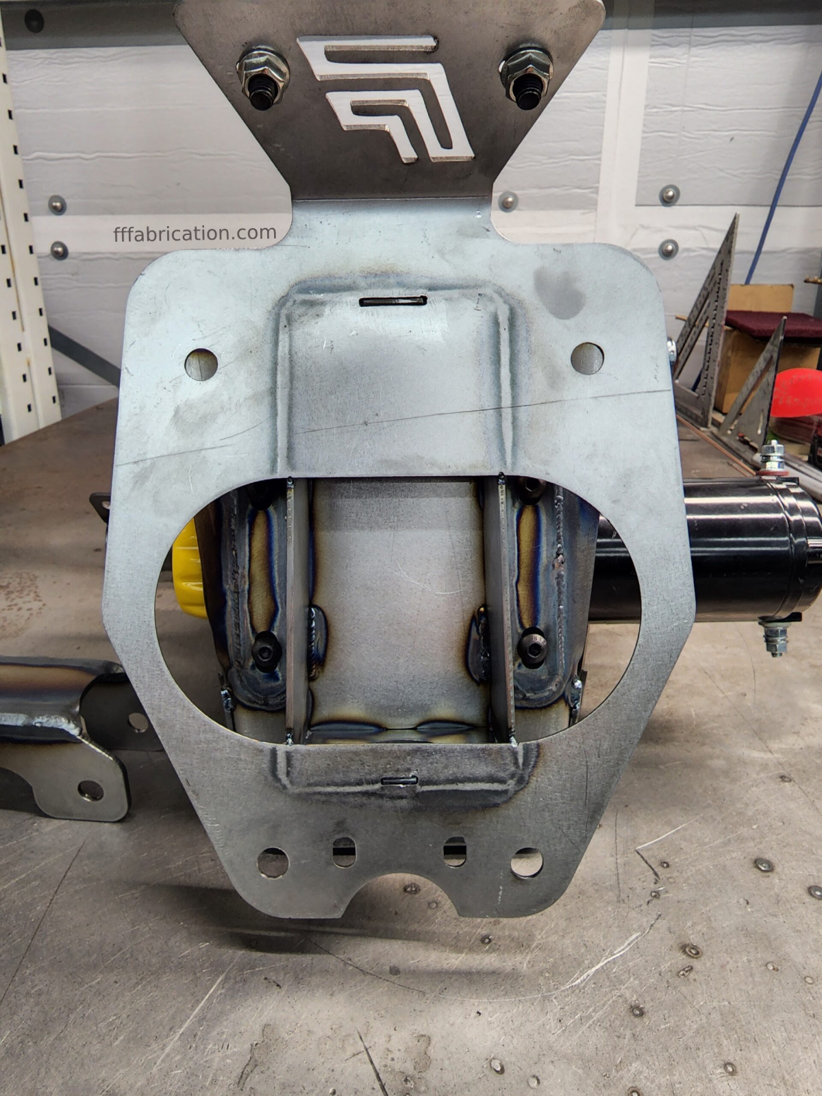 Metal mechanical component on a workshop floor with 'fffabrication.com' branding.